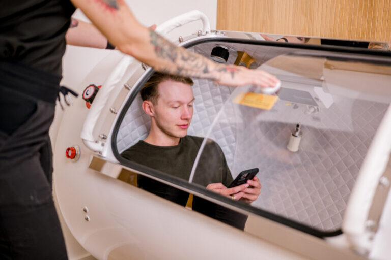 A man sitting and looking at his phone inside an oxygen chamber