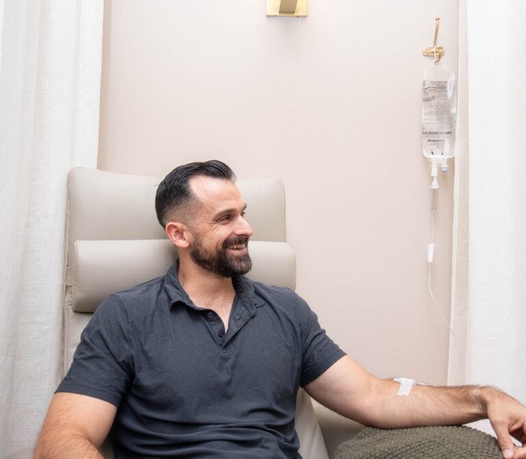 Smiling man sitting on a white couch while on IV therapy.